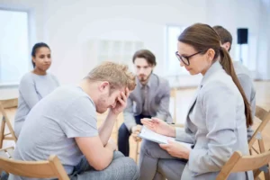 Distressed person in group therapy session with therapist and peers
