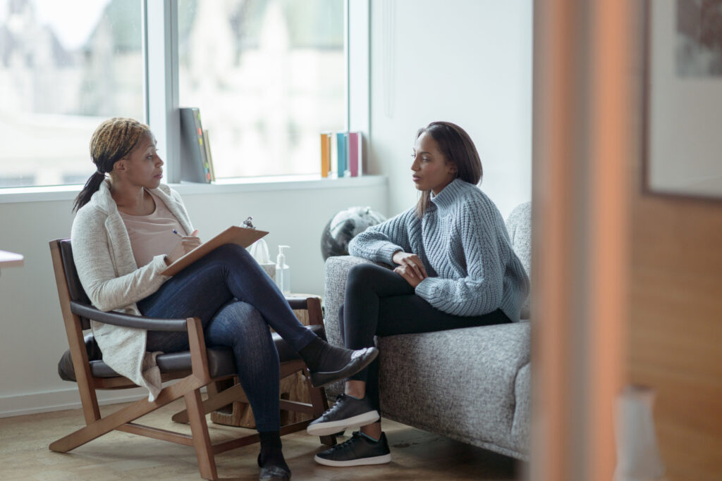 Therapist taking notes on clipboard while client talks in office