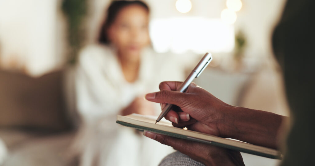 Therapist writing notes while client talks in background